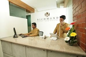 Een receptiebalie bij Richmond Hotel and Suites, met een computer, telefoon en een bloevas.