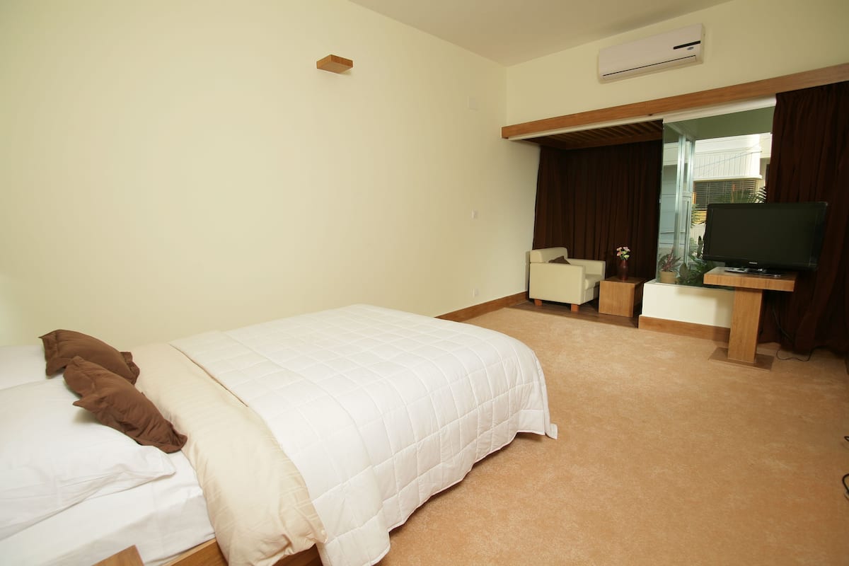 Habitación de hotel con cama, escritorio con televisor, una silla y un equipo de aire acondicionado.