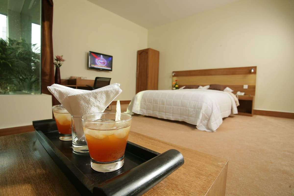 Habitación de hotel con cama, mesita de noche con vasos de té helado y un televisor en la pared.