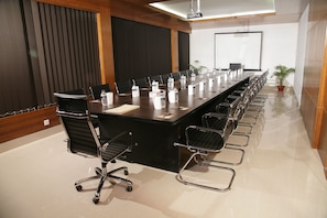 Een vergaderruimte met een lange tafel, stoelen, waterflesjes en een projectiescherm.