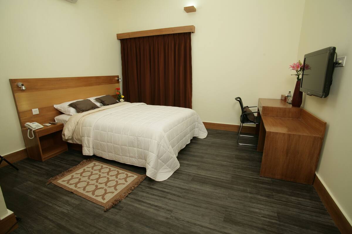 Habitación de hotel con cama, mesita de noche, lámpara, televisor y un pequeño escritorio con silla.