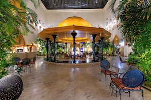 A spacious indoor area with a central open space, surrounded by seating arrangements and lush greenery.