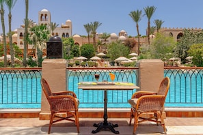 A poolside area with wicker chairs and a table, a pool with a metal railing, and a building with domed architecture in the background.