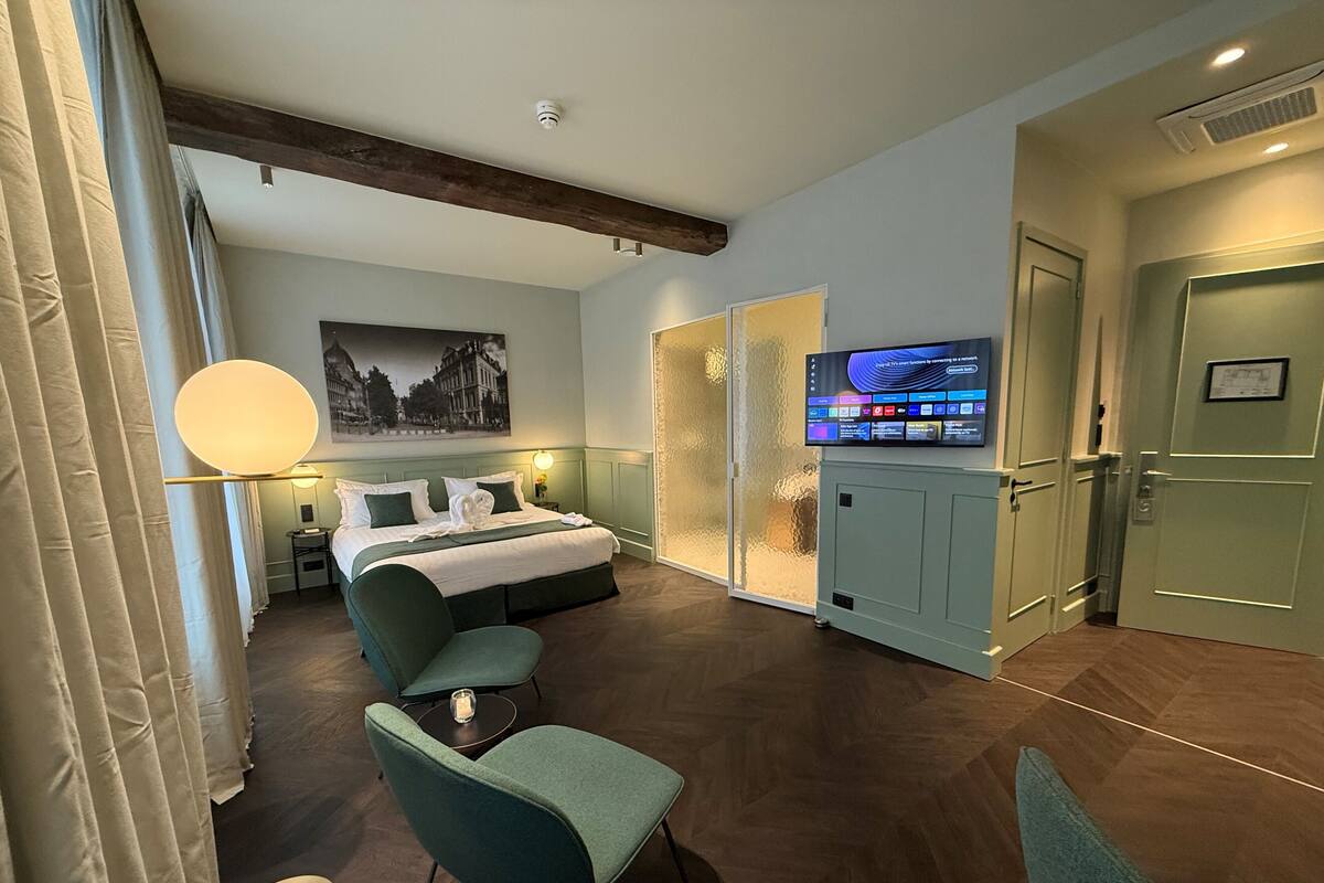 Een moderne hotelkamer met een bed, zithoek, televisie en een deur.