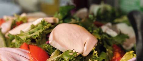 A bowl of salad with various vegetables and a piece of chicken, with condiments in the background.