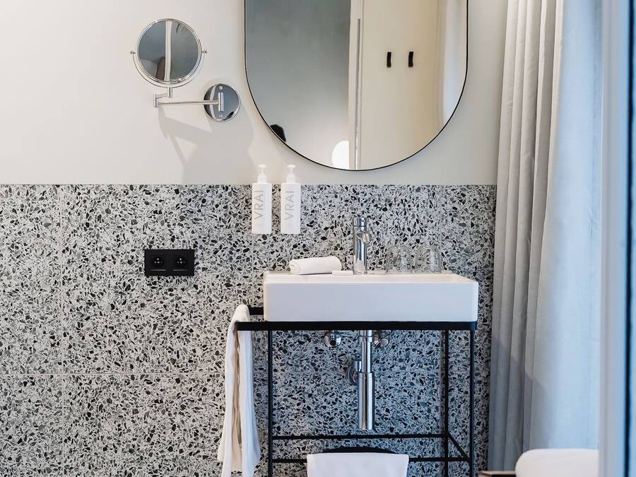 A modern bathroom with a granite backsplash, a round mirror, a sink with a towel rack, and a shower area.
