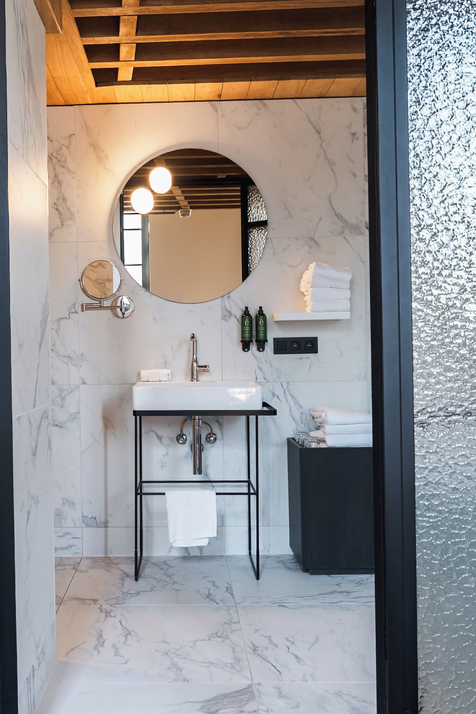 A modern bathroom with a marble sink, a round mirror, and a black vanity.