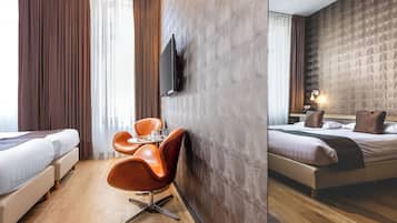 A hotel room with a bed, a desk with a chair, a TV mounted on the wall, and a window with curtains.