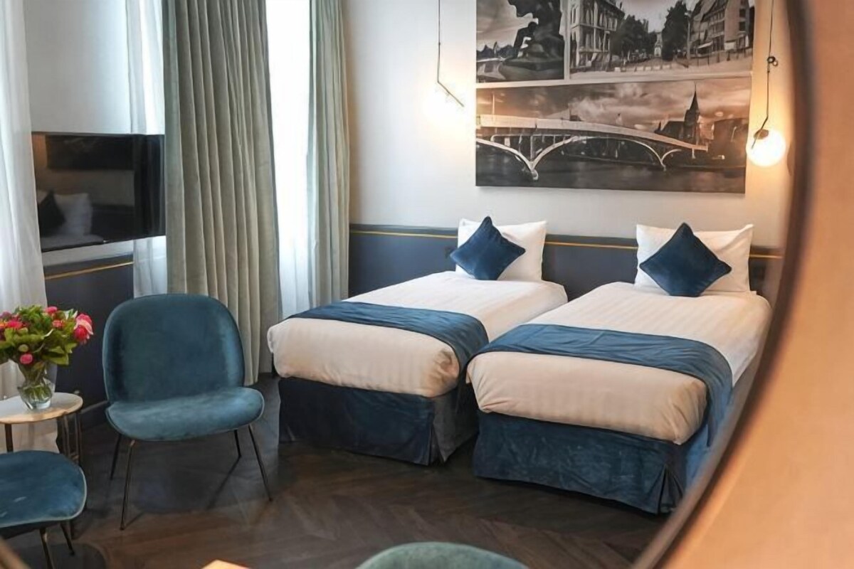 A hotel room with two beds, a TV, a desk with a chair, and a painting of a bridge.