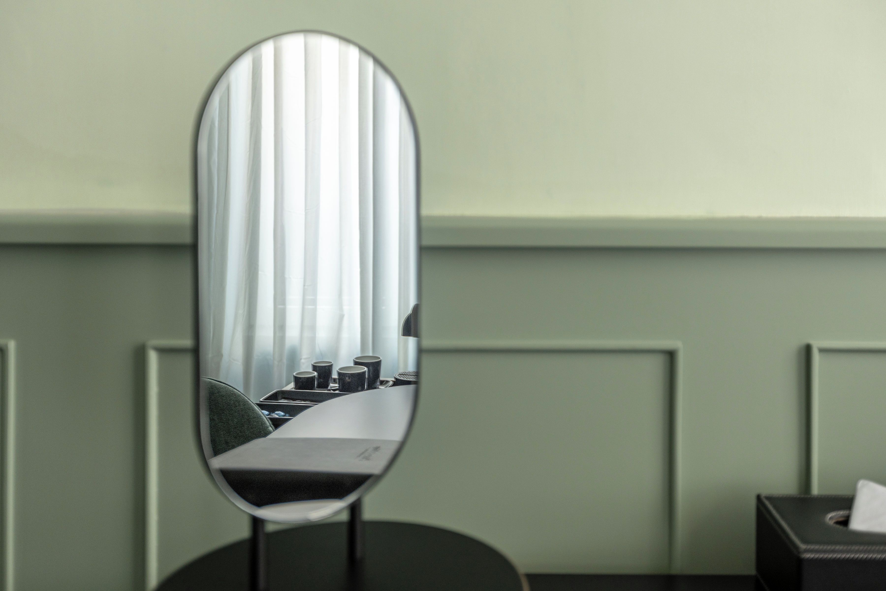 Un miroir reflétant une pièce, une table avec des tasses et une boîte de mouchoirs.
