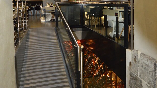 Een modern interieur met een trap naar een hoger niveau, een glazen scheiding en een zithoek met tafels en stoelen.