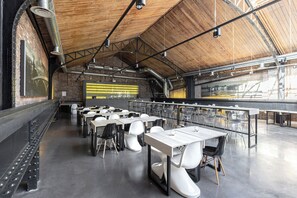 Un comedor amplio con techos altos y vigas a la vista, con mesas y sillas dispuestas para sentarse.