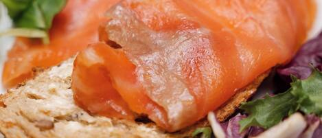 A plate with smoked salmon on a slice of bread, accompanied by a small piece of butter and a side salad.