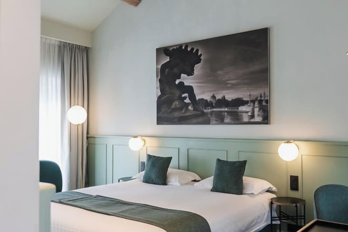 Habitación de hotel con cama, dos lámparas de noche, cabecera, un cuadro en la pared y vista a un cuerpo de agua.