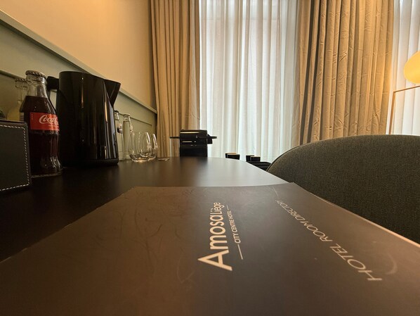 Habitación de hotel con una mesa dispuesta para comer, una botella de Coca-Cola y un vaso. La habitación tiene vistas de la ciudad a través de cortinas traslúcidas.
