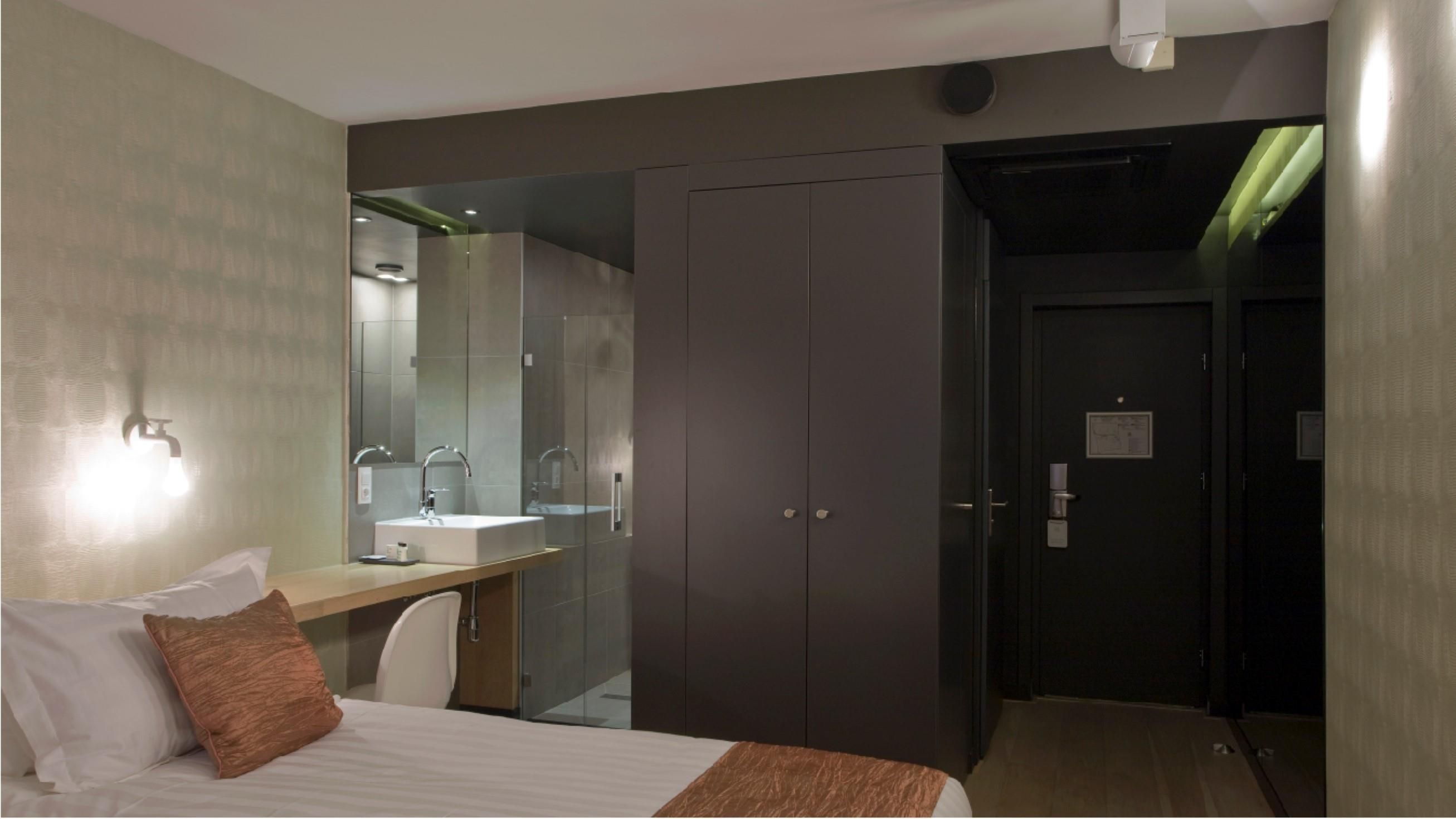 Habitación de hotel con cama, mesita de noche, espejo, armario y baño con lavabo y ducha.