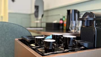 Een koffieapparaat met vier zwarte kopjes op een dienblad, een magnetron en een waterkoker op een keukentafel.
