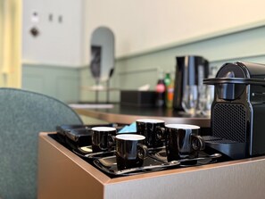 Une machine à café avec quatre tasses noires posées sur un plateau, un four à micro-ondes et une bouilloire sur un plan de travail de cuisine.