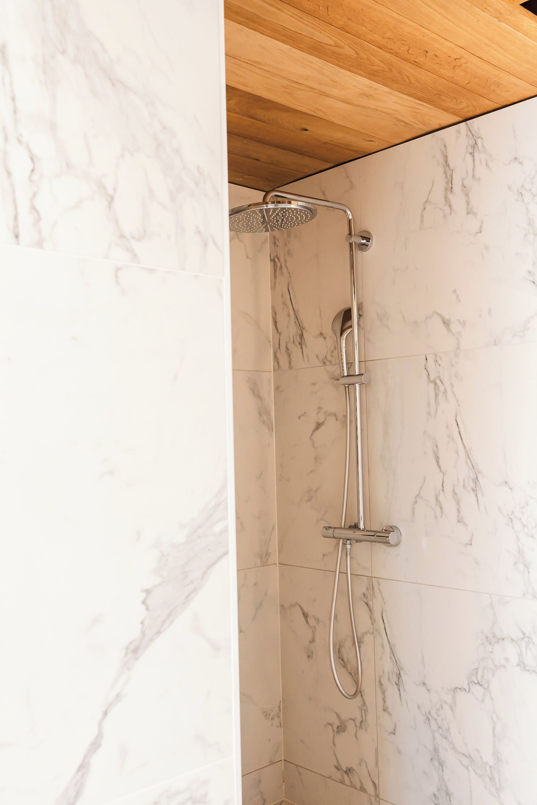 Een douche met een handdouche en een kraan op de muur in een badkamer met marmeren wanden.