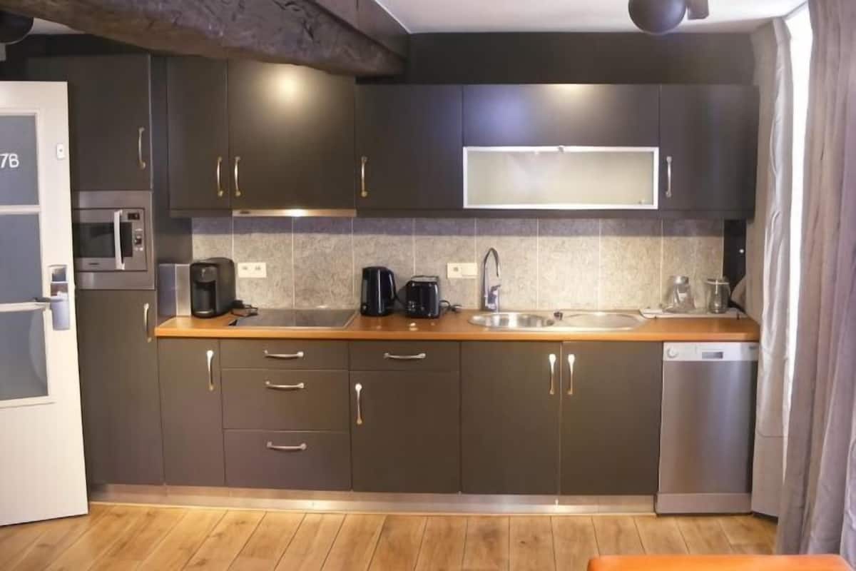 A modern kitchen with dark cabinets, a wooden countertop, a built-in microwave, a coffee maker, and a dishwasher.