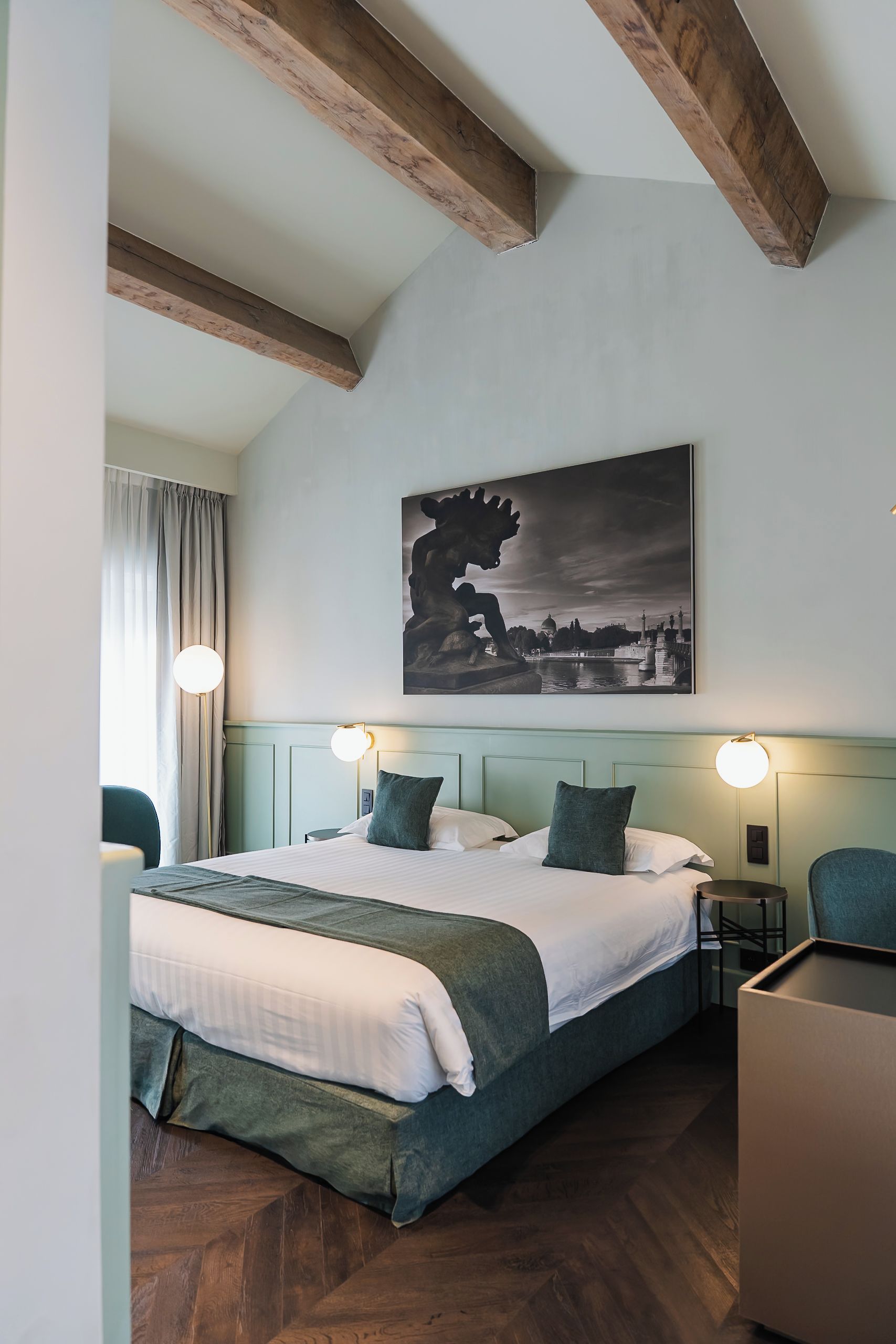 A hotel room with a large bed, two bedside tables, a chair, and a painting on the wall.