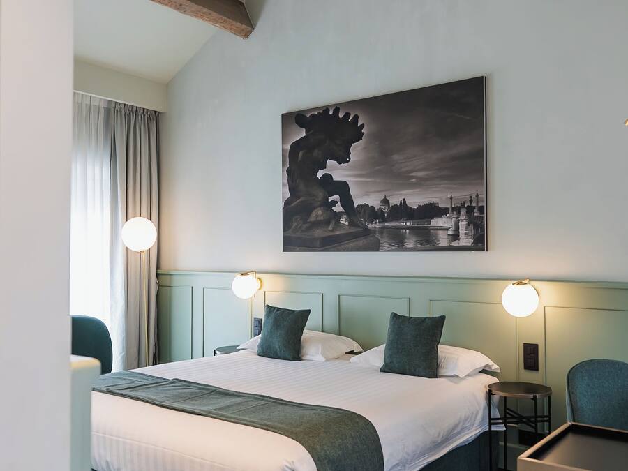 Una habitación de hotel con una cama grande, dos mesitas de noche, una silla y un cuadro en la pared.