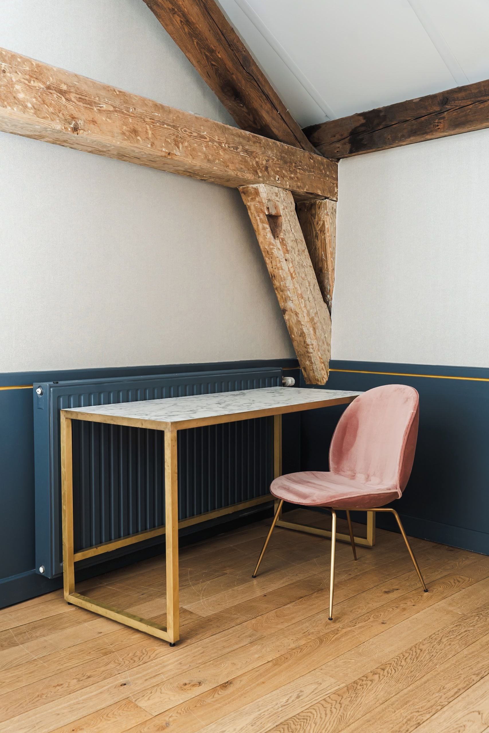 Una habitación con un escritorio de madera, una silla rosa y vigas de madera a la vista.