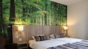 Hotelkamer met een groot bed, twee nachtkastjes, een stoel en een groot wanddecor met een bosmotief.