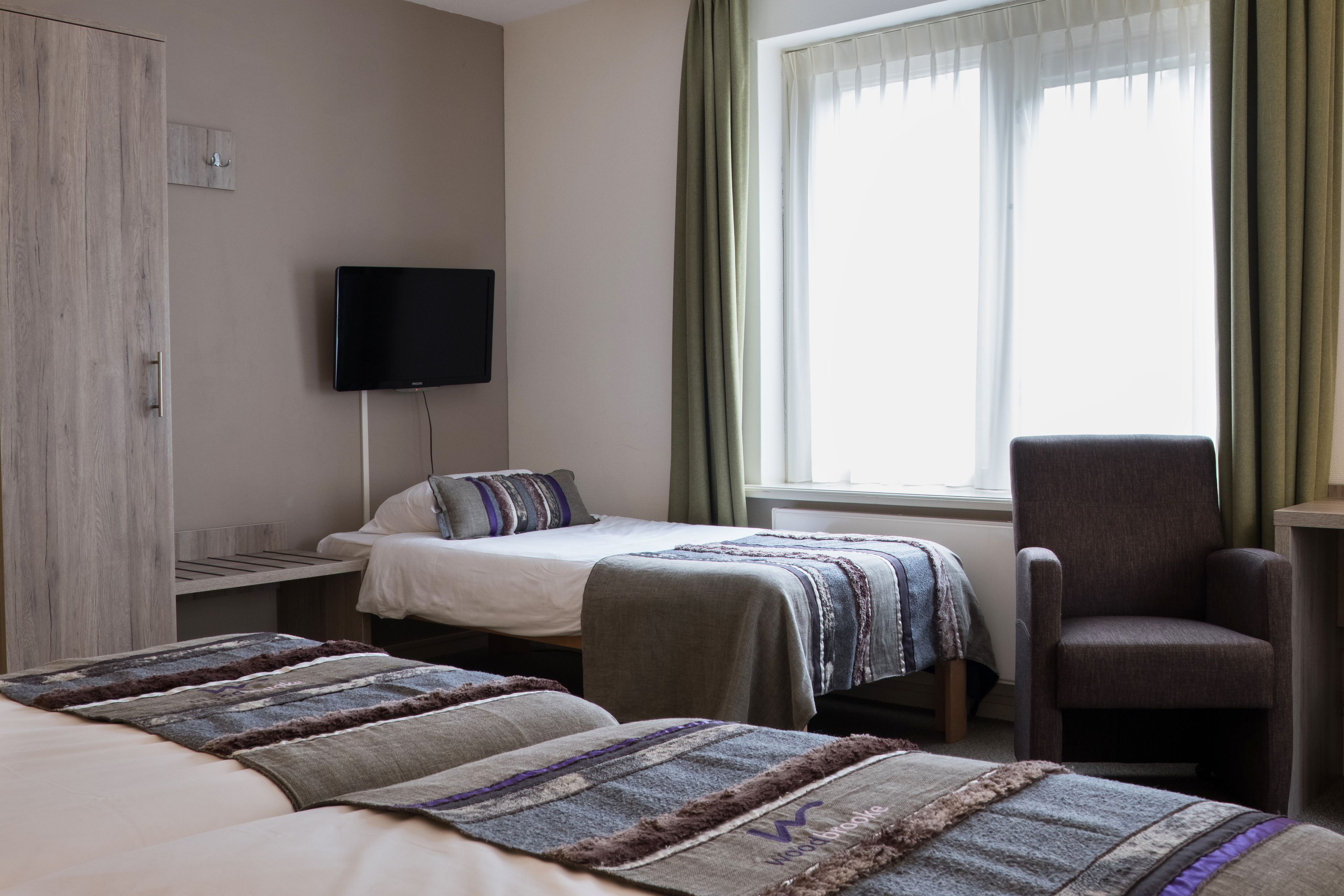 A hotel room with two beds, a TV, a chair, and a window with curtains.
