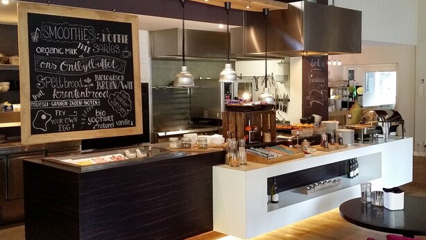 Een modern café interieur met een prikbord waarop een menukaart staat met smoothies, koffie en biologische melk.
