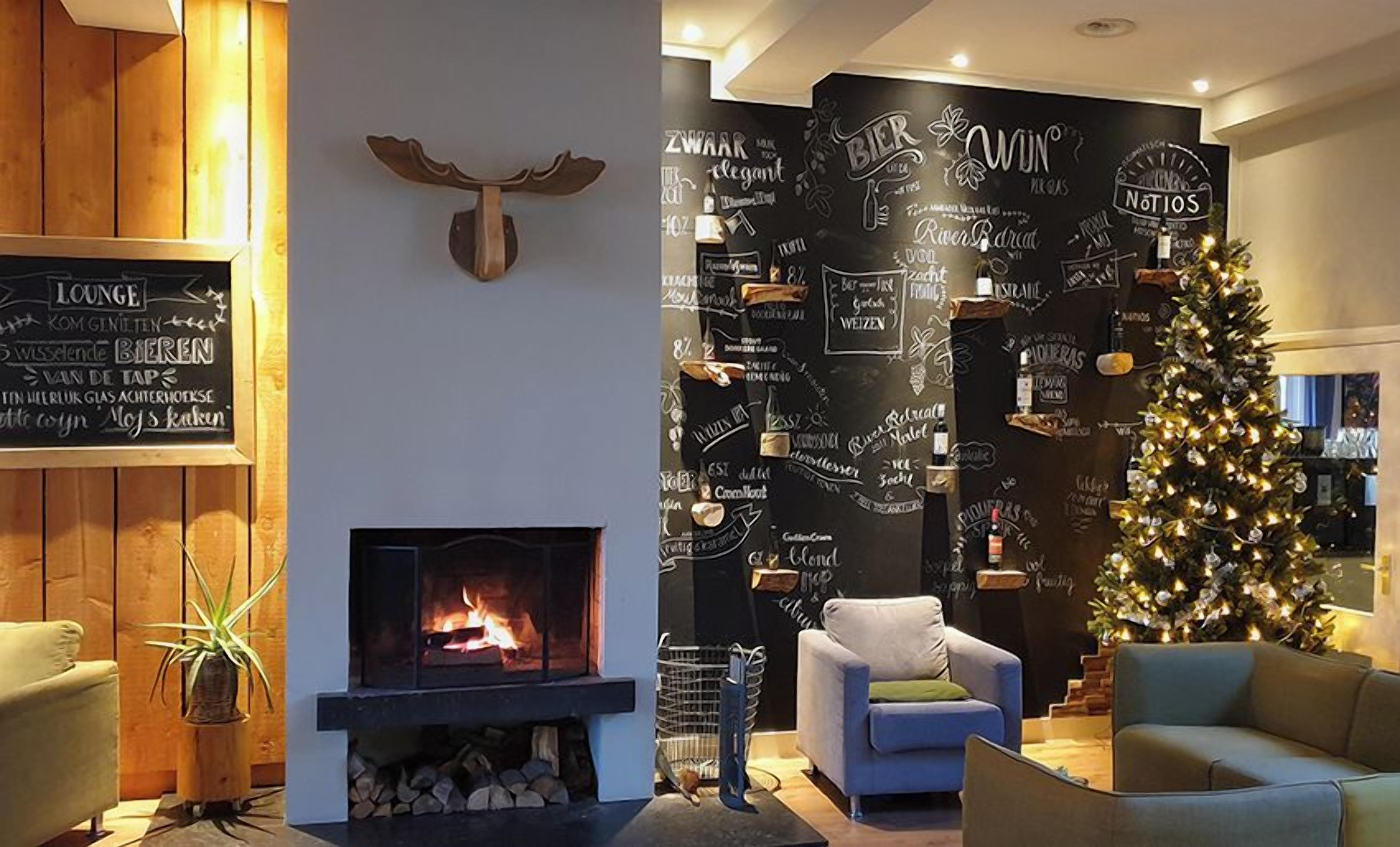 A cozy lounge area with a fireplace, a Christmas tree, and a wall decorated with beer-related phrases.