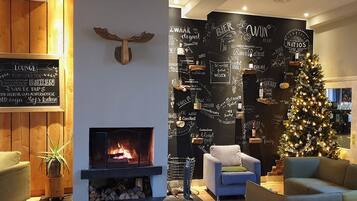 A cozy lounge area with a fireplace, a Christmas tree, and a wall decorated with beer-related phrases.