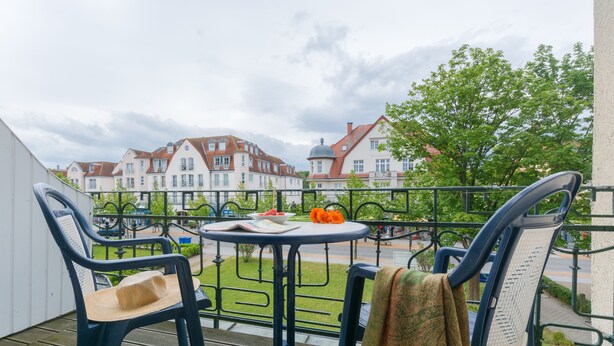 Een balkon met twee stoelen, een tafeltje en een uitzicht op huizen op de achtergrond.