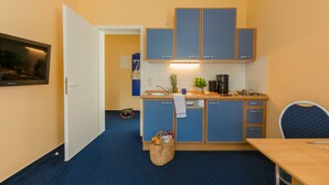 Een compacte keuken met blauwe kastjes, een houten tafel en een stoel. Een mand met een handdoek hangt aan de deur.