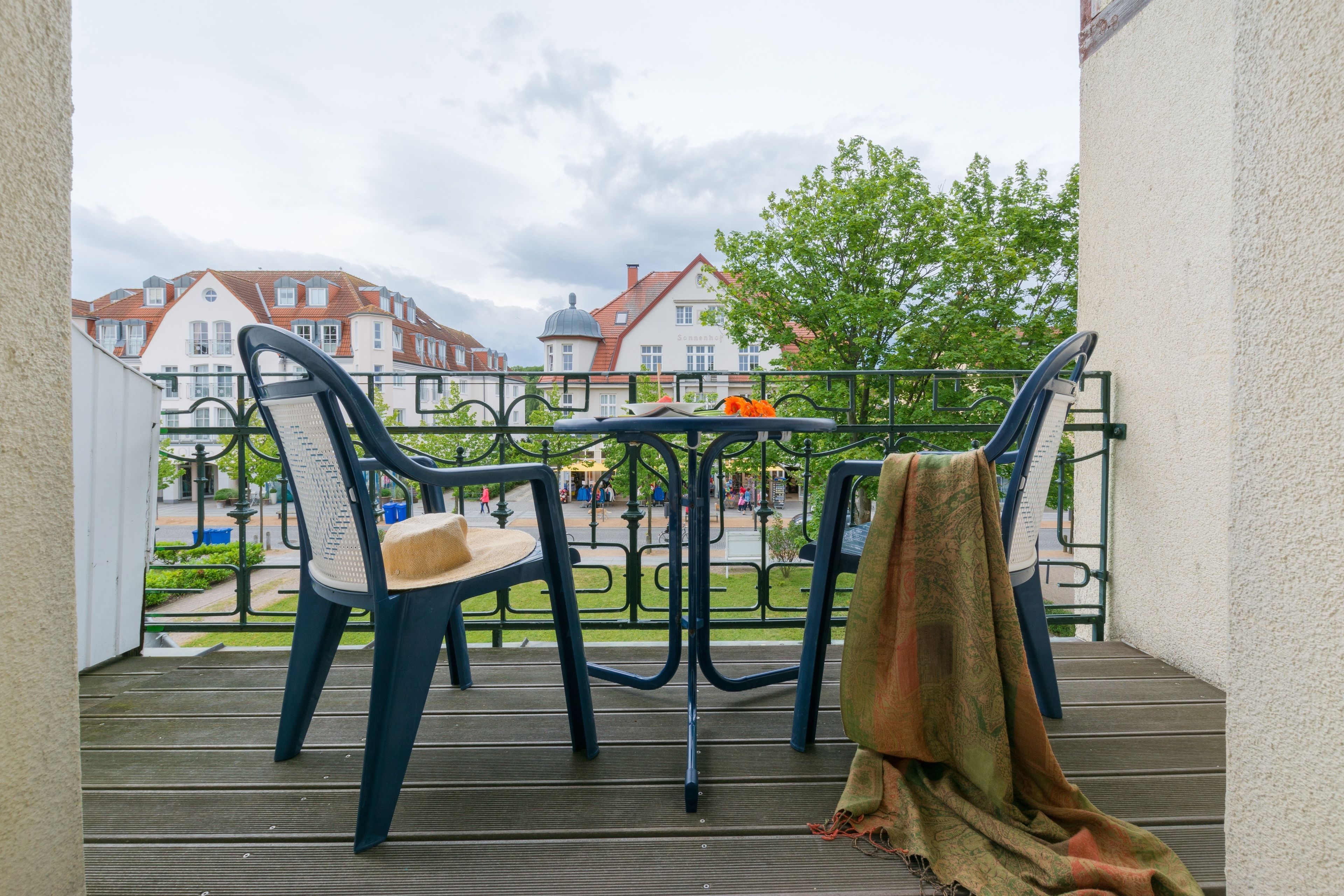 Un balcon avec deux chaises et une table, donnant sur une cour intérieure bordée de bâtiments et agrémentée d’un arbre.