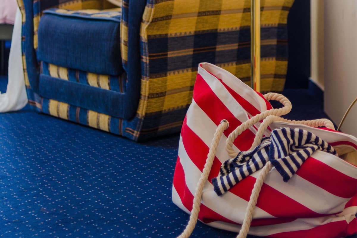 Ein Zimmer mit einem Karo-Sessel, einer Lampe und einer Streifen-Tasche auf einem blauen Teppich.
