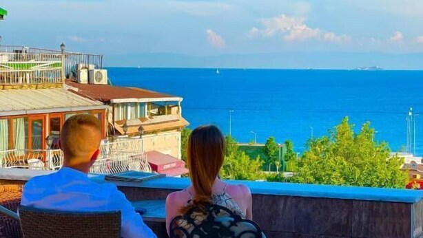A couple seated at an outdoor table with a view of the sea and buildings in the background. - Hotel Rose Bouquets (Istanbul)