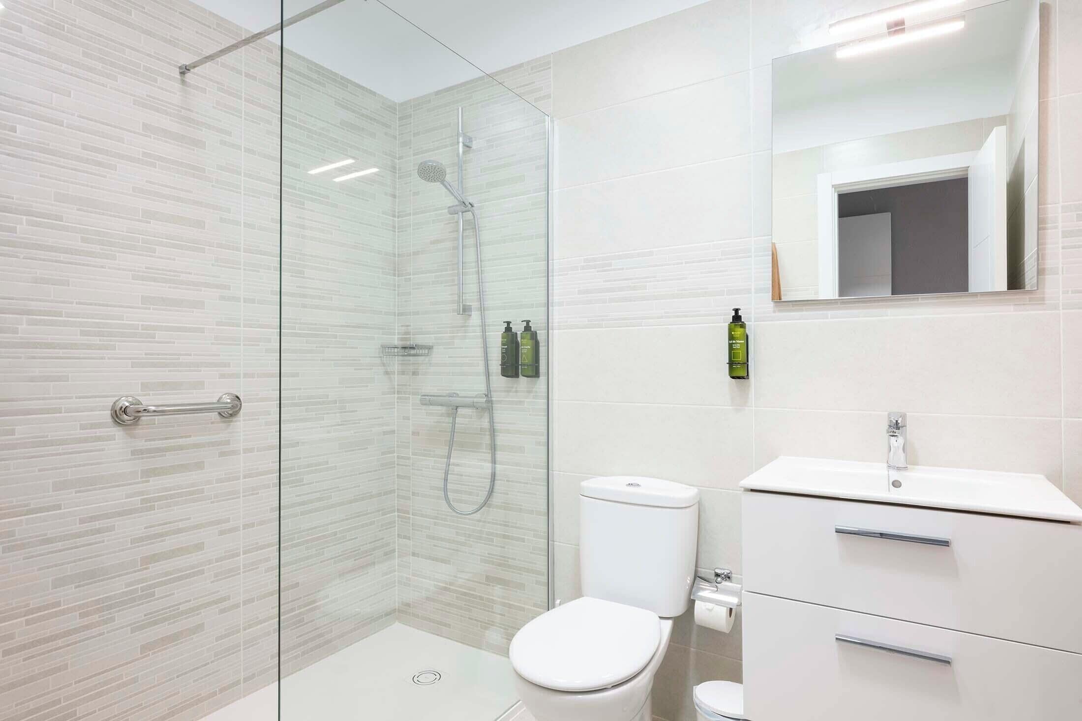 Une salle de bain moderne avec une douche à parois de verre, des toilettes blanches et un meuble-lavabo avec un miroir.