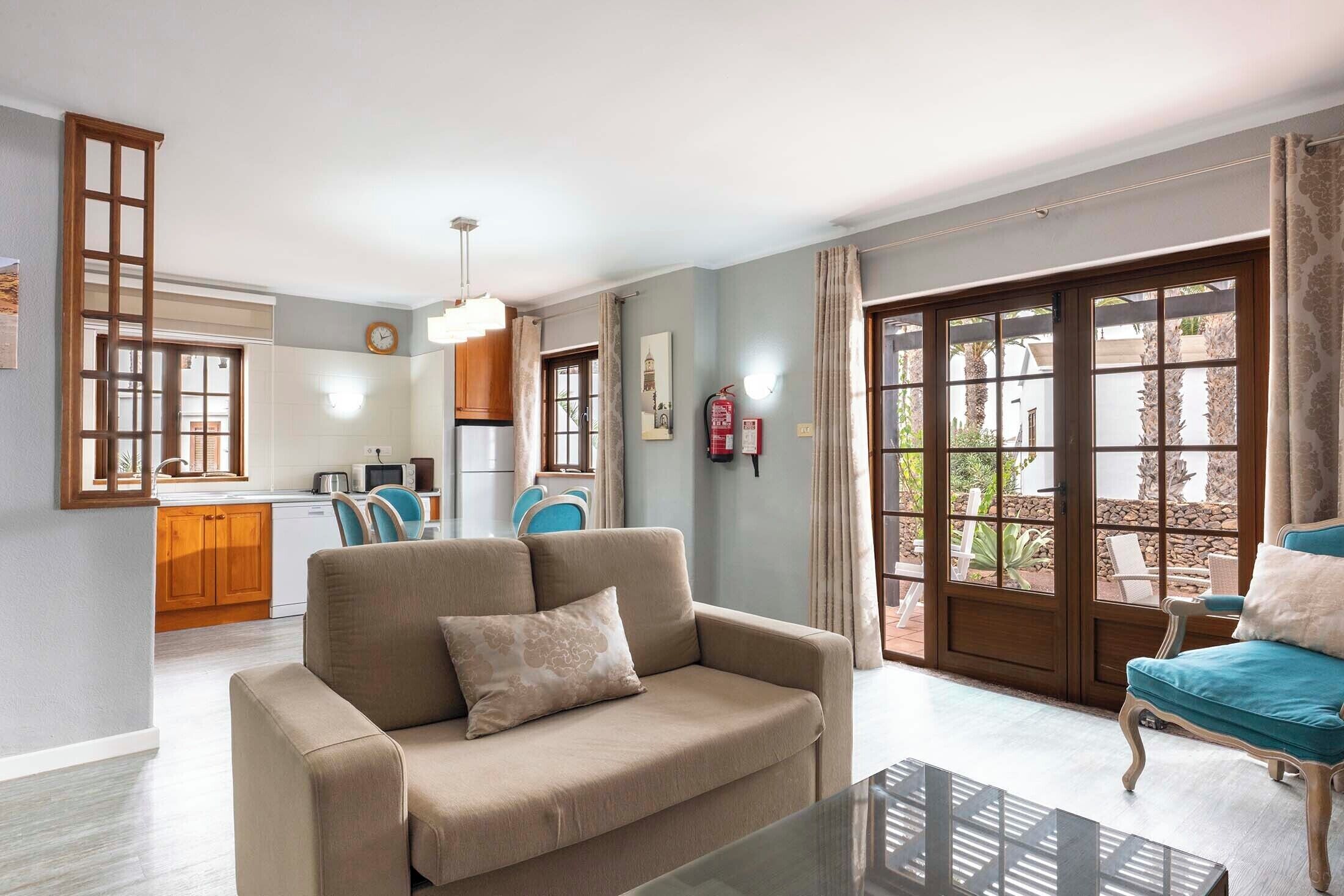A living room with a sofa, a glass coffee table, and a view of the kitchen and outdoor area.