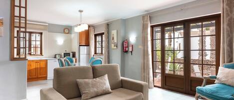 A living room with a sofa, a glass coffee table, and a view of the kitchen and outdoor area.