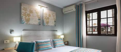 A hotel room with a bed, bedside tables, a desk, and a window with curtains.