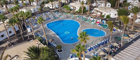 Ett semesterhotell med en central pool omgiven av solstolar och palmer.