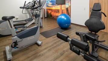 Un gimnasio con equipo de ejercicio, una pelota de ejercicios azul y un televisor instalado en la pared.