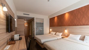 Habitación de hotel con dos camas, cabecera de madera, televisor de pantalla plana, escritorio con lámpara y espejo.
