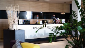 Una recepción con un mural de un horizonte urbano, una pantalla digital y una máquina de café.