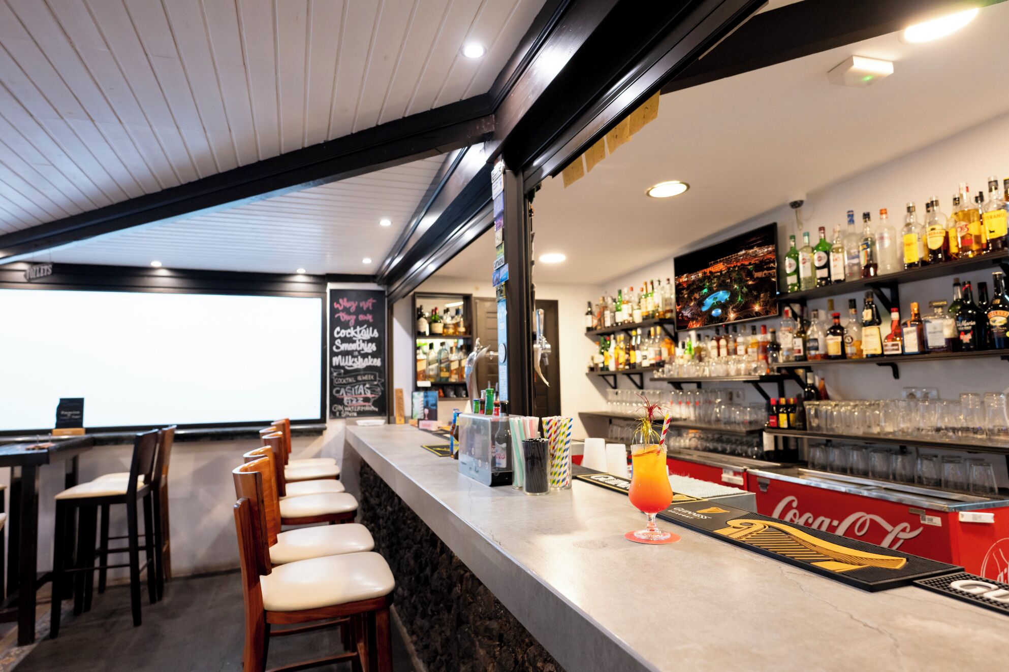A bar area with a counter, bar stools, shelves of liquor bottles, and a chalkboard menu.
