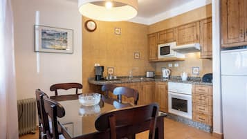A modern kitchen with wooden cabinets, a microwave, a stove, and a dining area with a glass table and chairs.