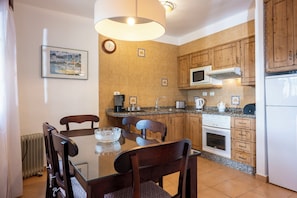 Una cocina moderna con armarios de madera, un microondas, una estufa y un comedor con mesa y sillas de vidrio.
