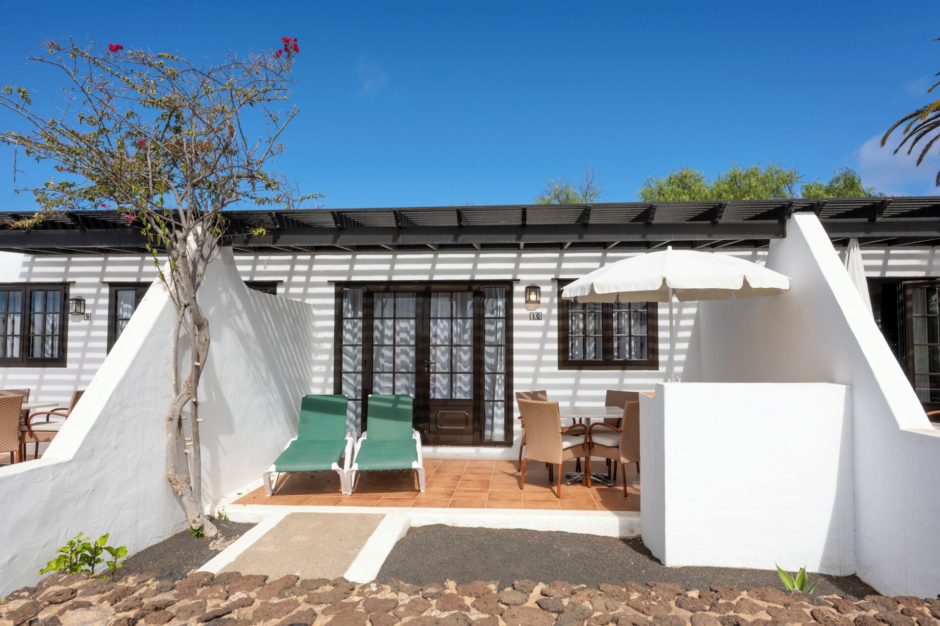 A building with a white exterior, a covered patio with green chairs, and a white umbrella.