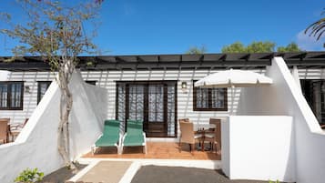A building with a white exterior, a covered patio with green chairs, and a white umbrella.